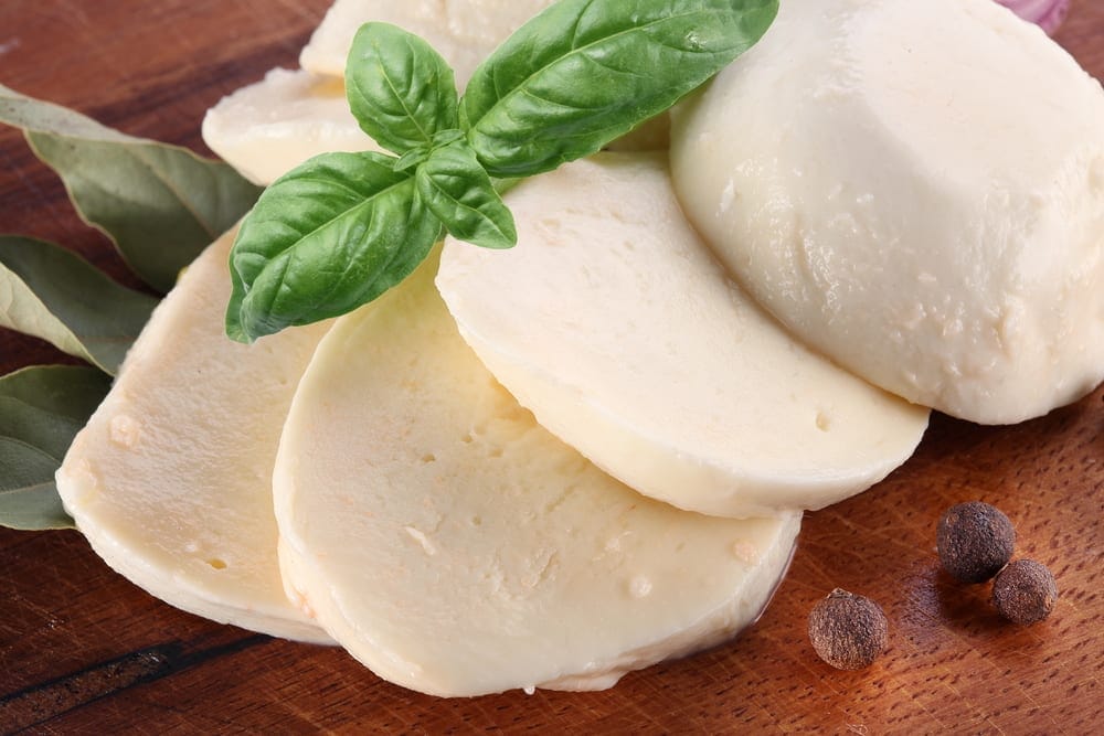 sliced buffalo mozzarella on a board with a sprig of basil. Learn all about what makes this cheese so delicious!