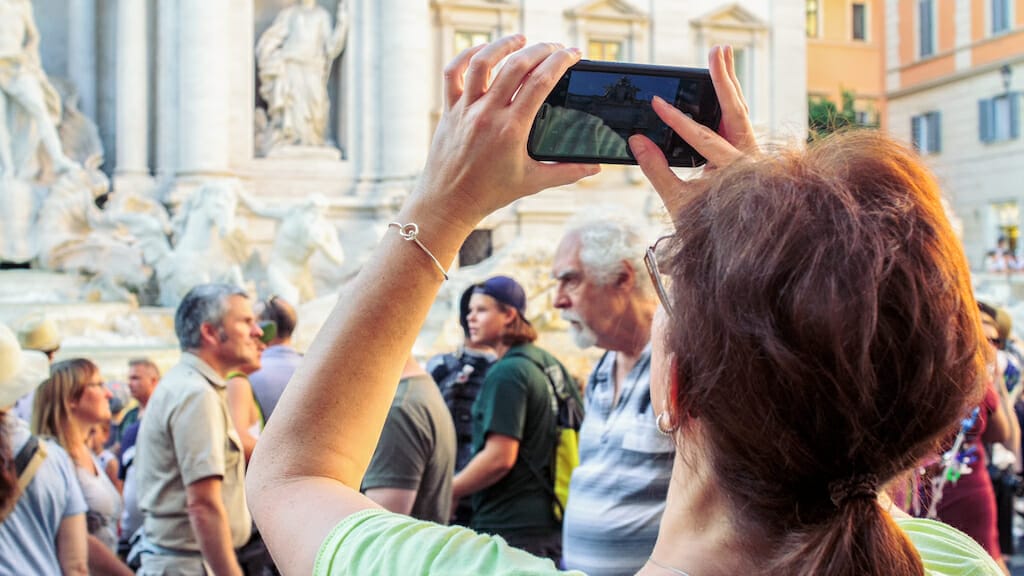 A woman tourist in Rome takes a photo of the Trevi Fountain during the day with her phone