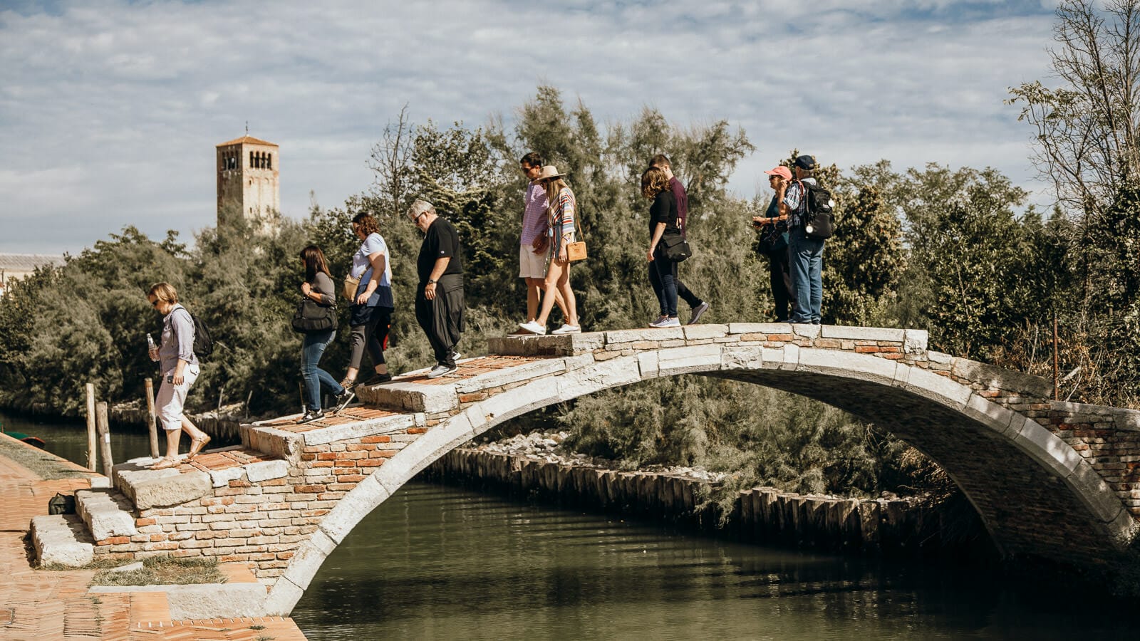 Small group of tourists climb over a narrow bridge over a Venetian canal
