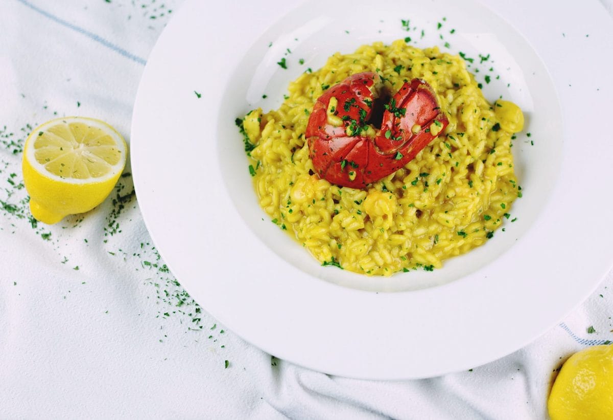 A dish of yellow Italian risotto alla milanese with a shrimp or lobster on top