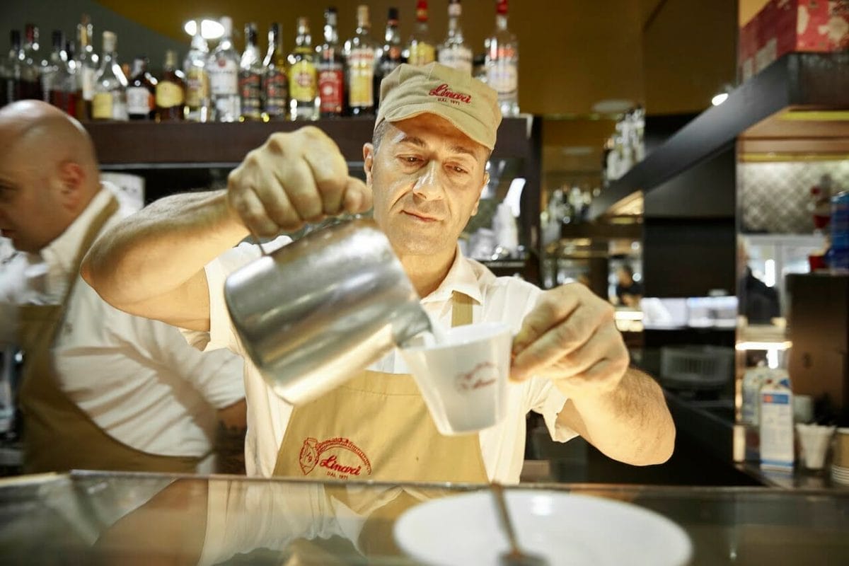 Barman pours heated milk into a tiny coffee or espresso cup in Rome.