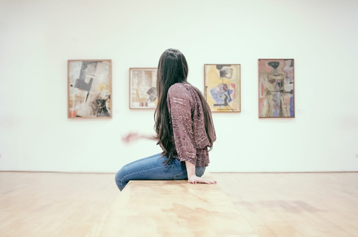 Woman sitting on a bench in a museum looking at works of art.