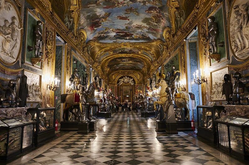 A view inside one of the prominent halls of the The Royal Palace of Turin displaying statues of knights on horses and a ceiling with a detailed painting of angels.