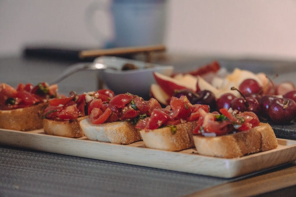 Bruschetta with cherry tomatoes and basil on bread next to a tray of cherries, apples, and olives.