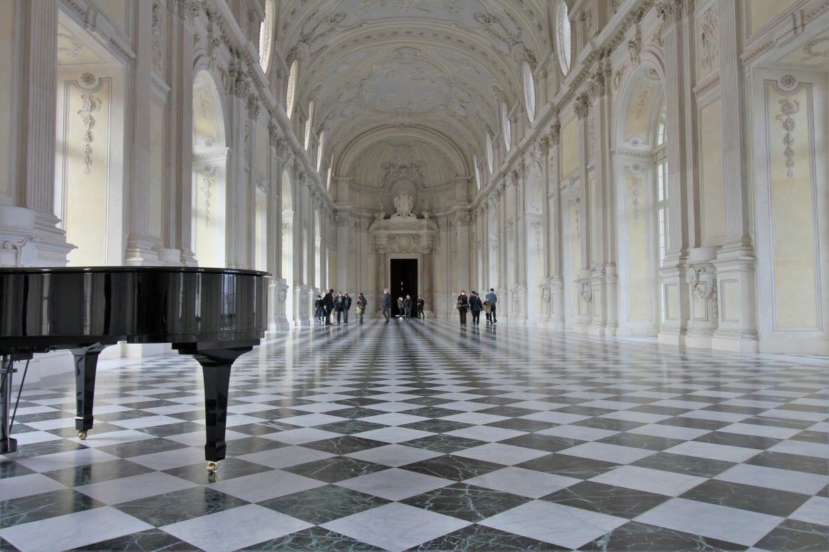 A view inside a main hall of the Venaria Reale showing a black and white checkered floor and a grand piano.