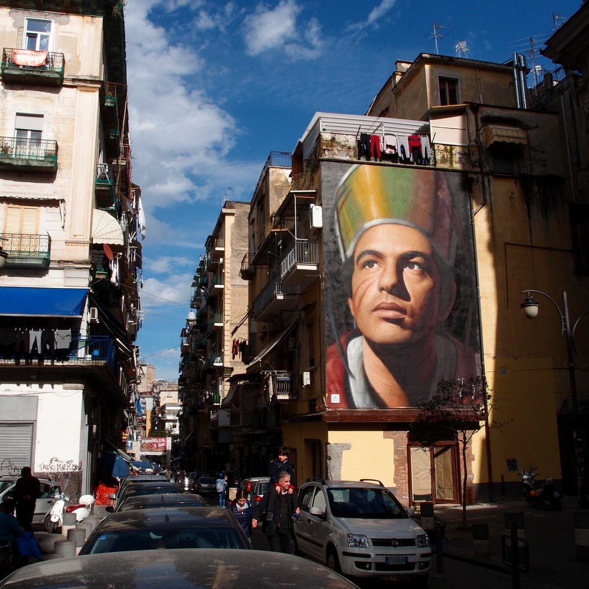 A view of a street in Naples, Italy, displaying street art from the artist Jorit.