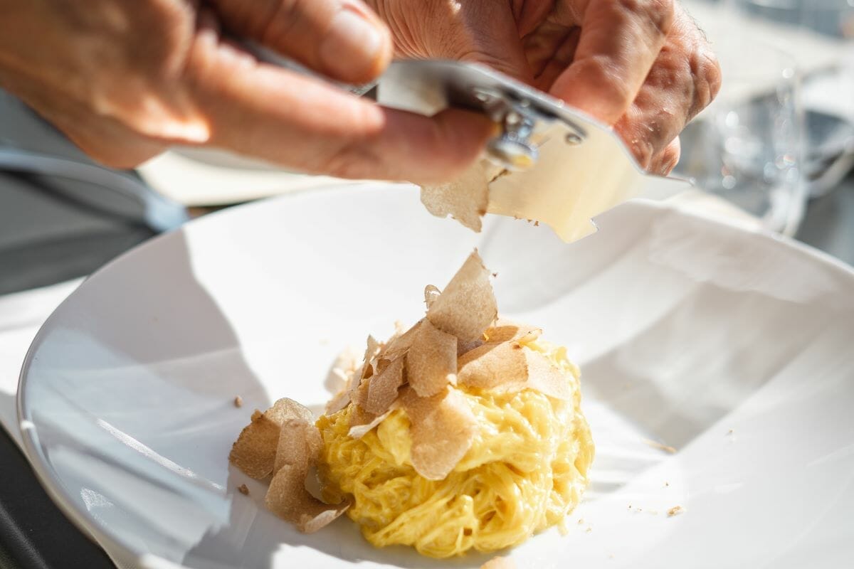 White truffles being shaved on top of a bowl of fresh pasta