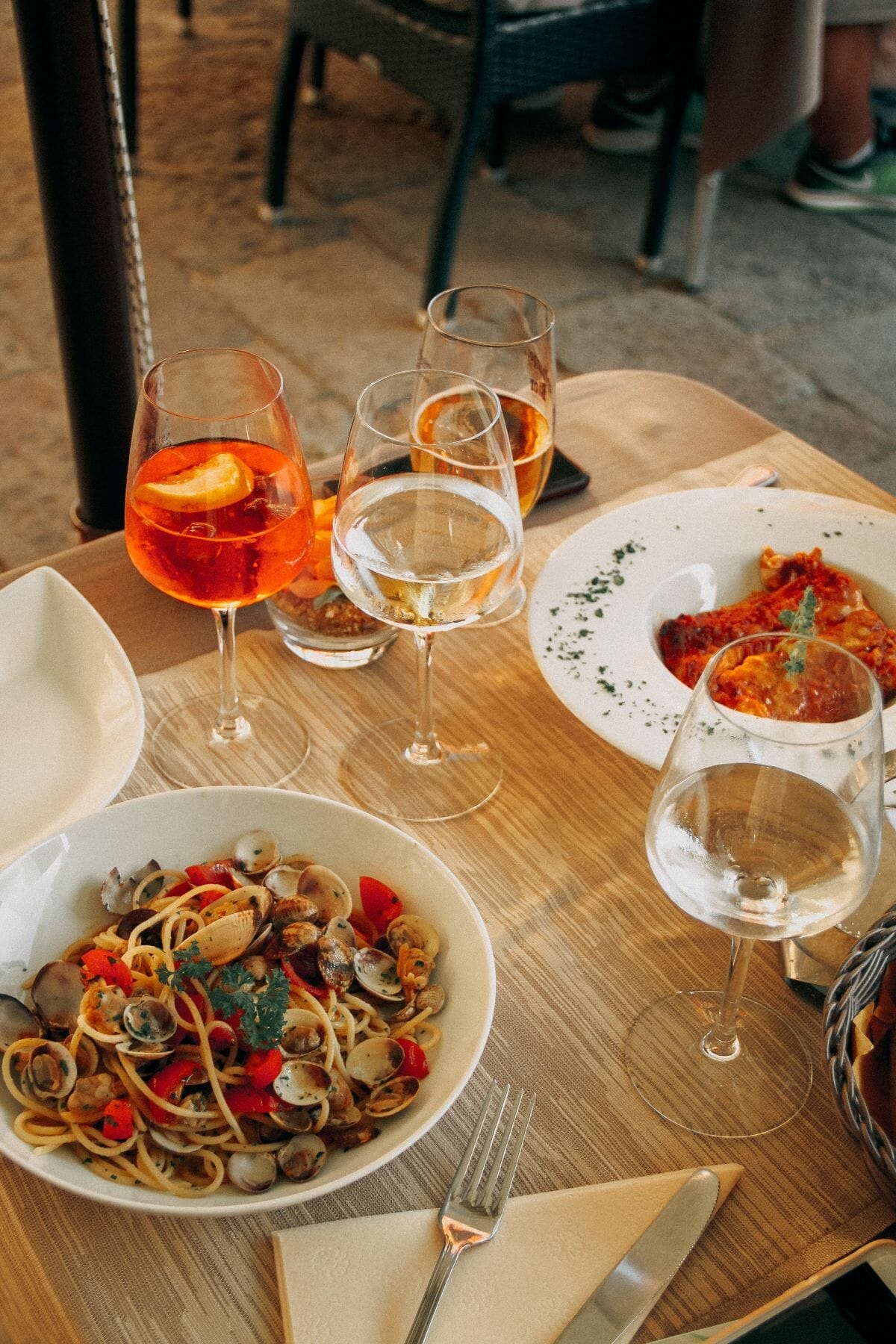 Plates of seafood pasta surrounding by glasses of wine and Aperol Spritz