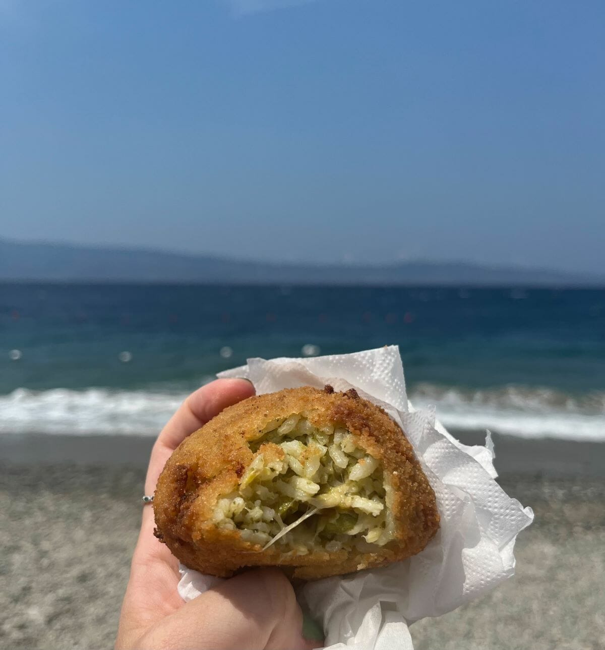 A ball of fried rice, arancini, with views of the ocean in the back